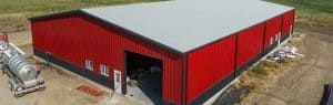 Aerial view of a large red metal agricultural building with a gray roof, showcasing durability and design relevant to Central States Metal from Stoneburner, ideal for farming and storage needs.